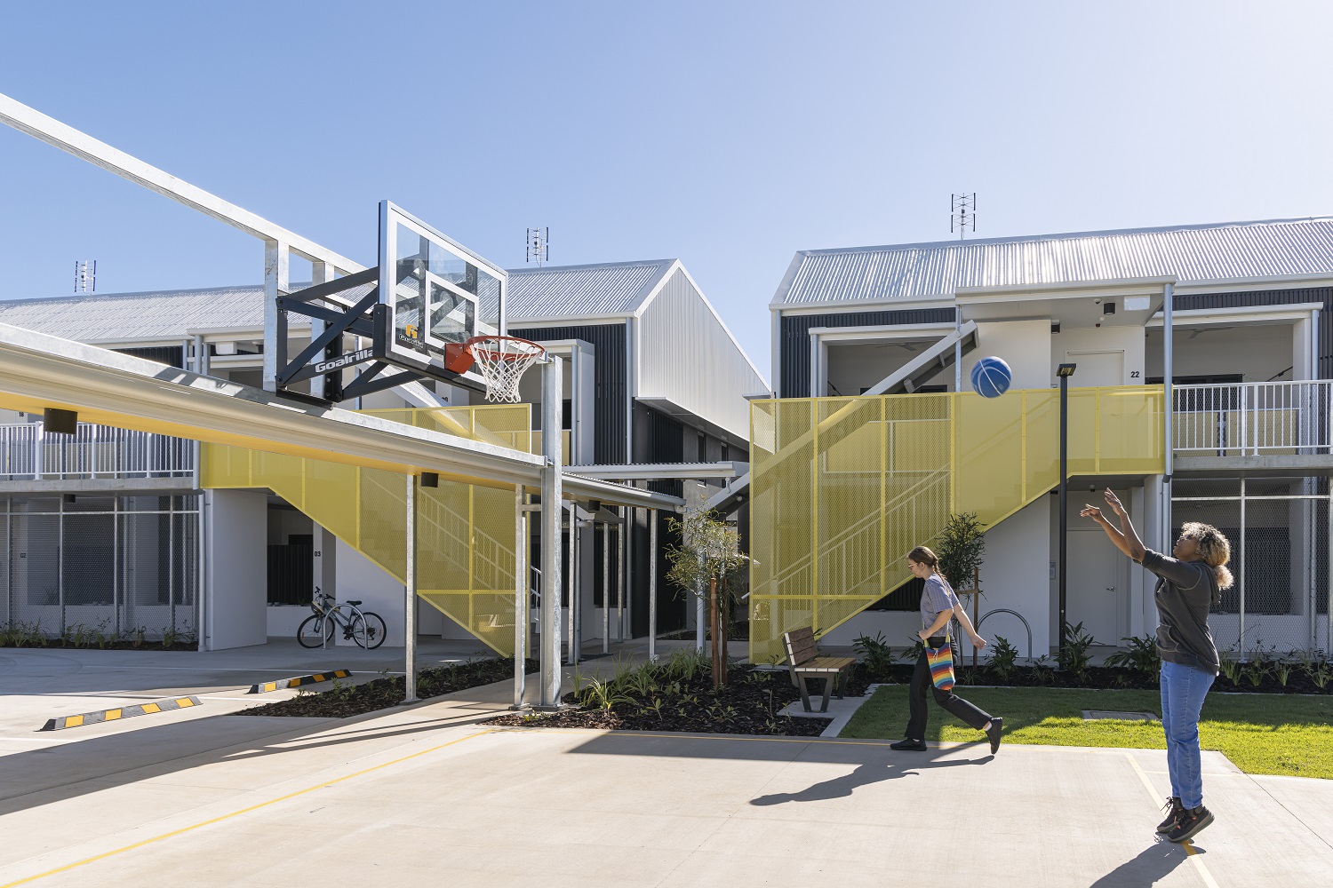 young person walking and other playing basketball in front of the youth foyer